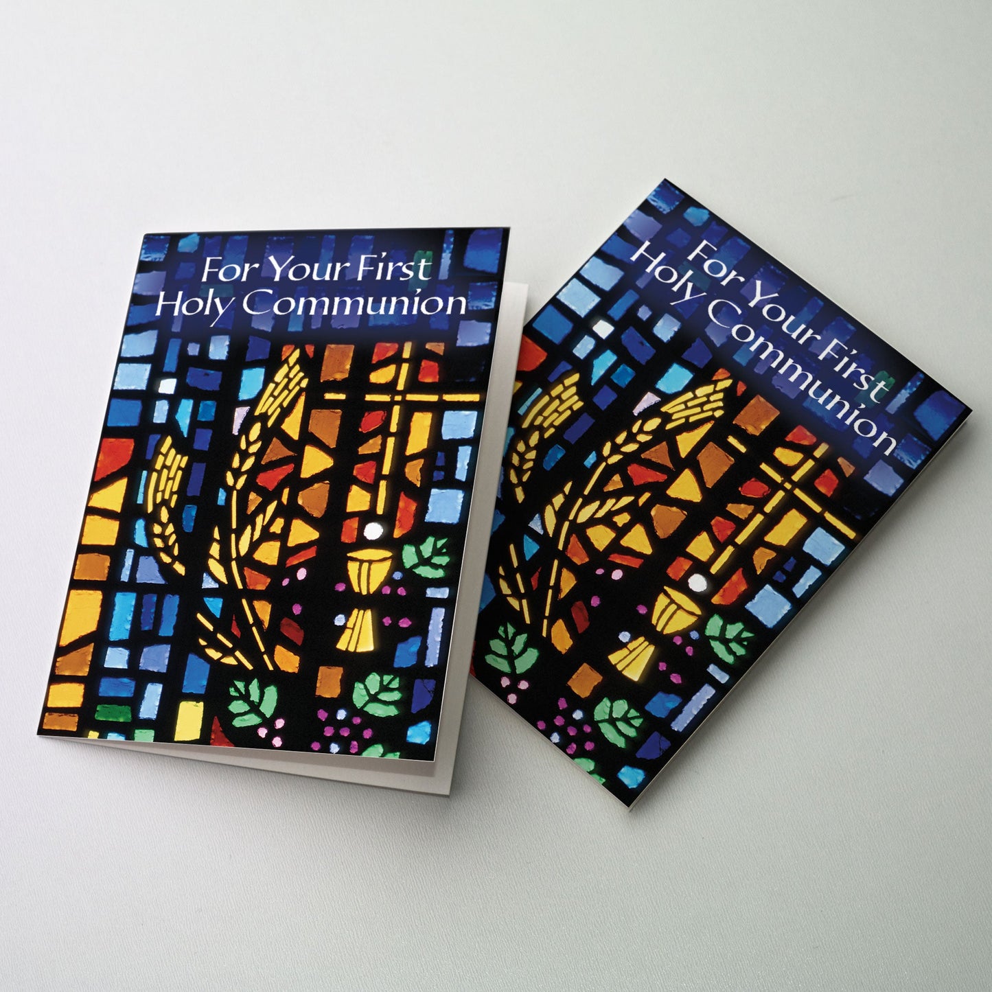 Stained glass window image of a chalice and host surrounded by a cross, shocks of wheat and clusters of grapes.