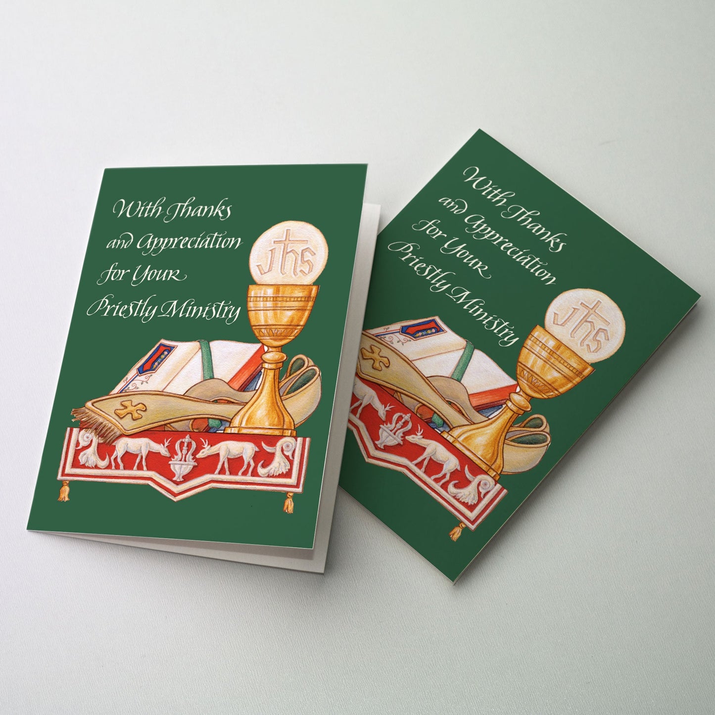 Chalice and host, stole and gospel book on an altar. The altar is covered with a red cloth displaying the image of two deer drinking from the fountain of life.