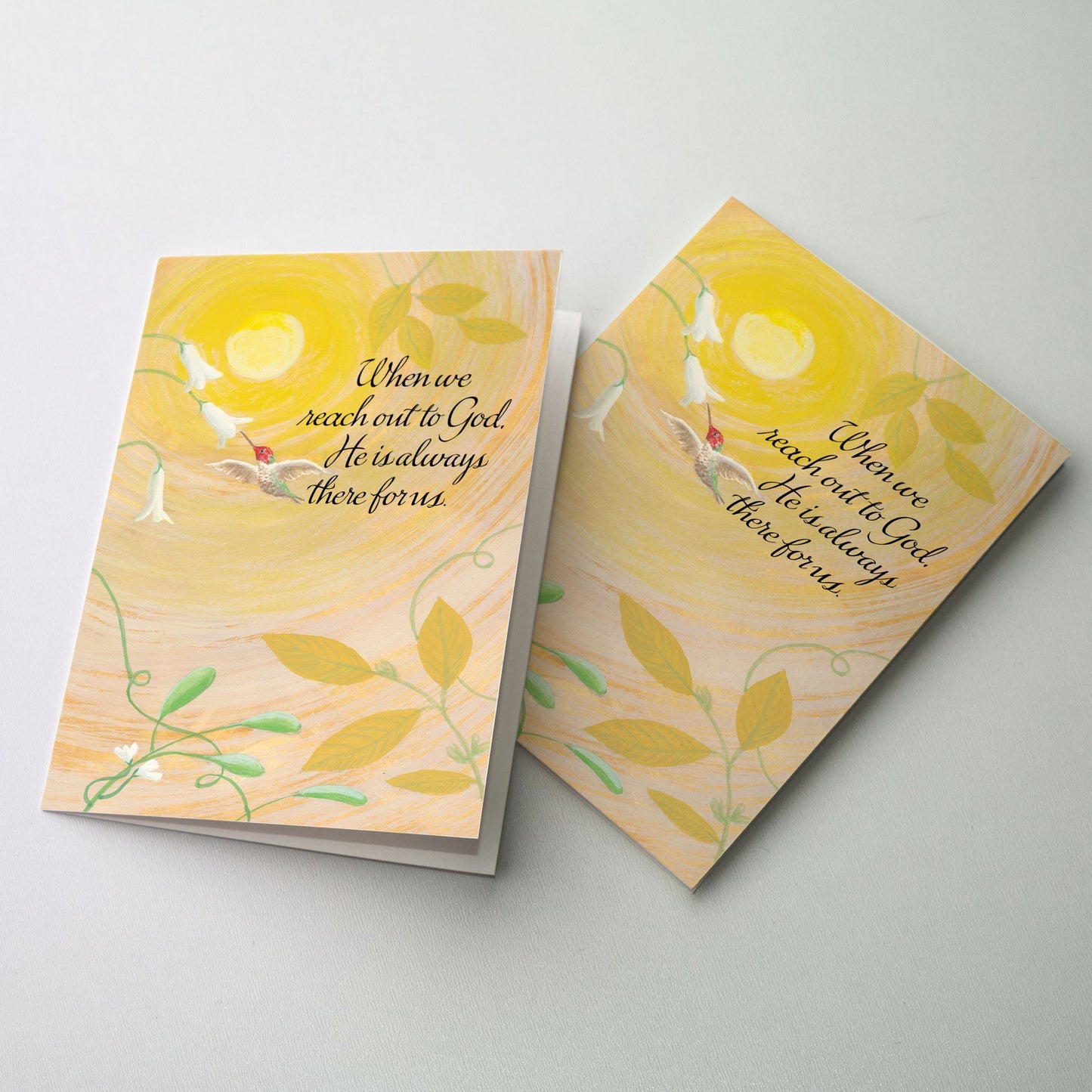 A red and green hummingbird gathers nectar from the blossoms of white flowers. A golden sun is in the background emanating rings of light in a peach colored sky.