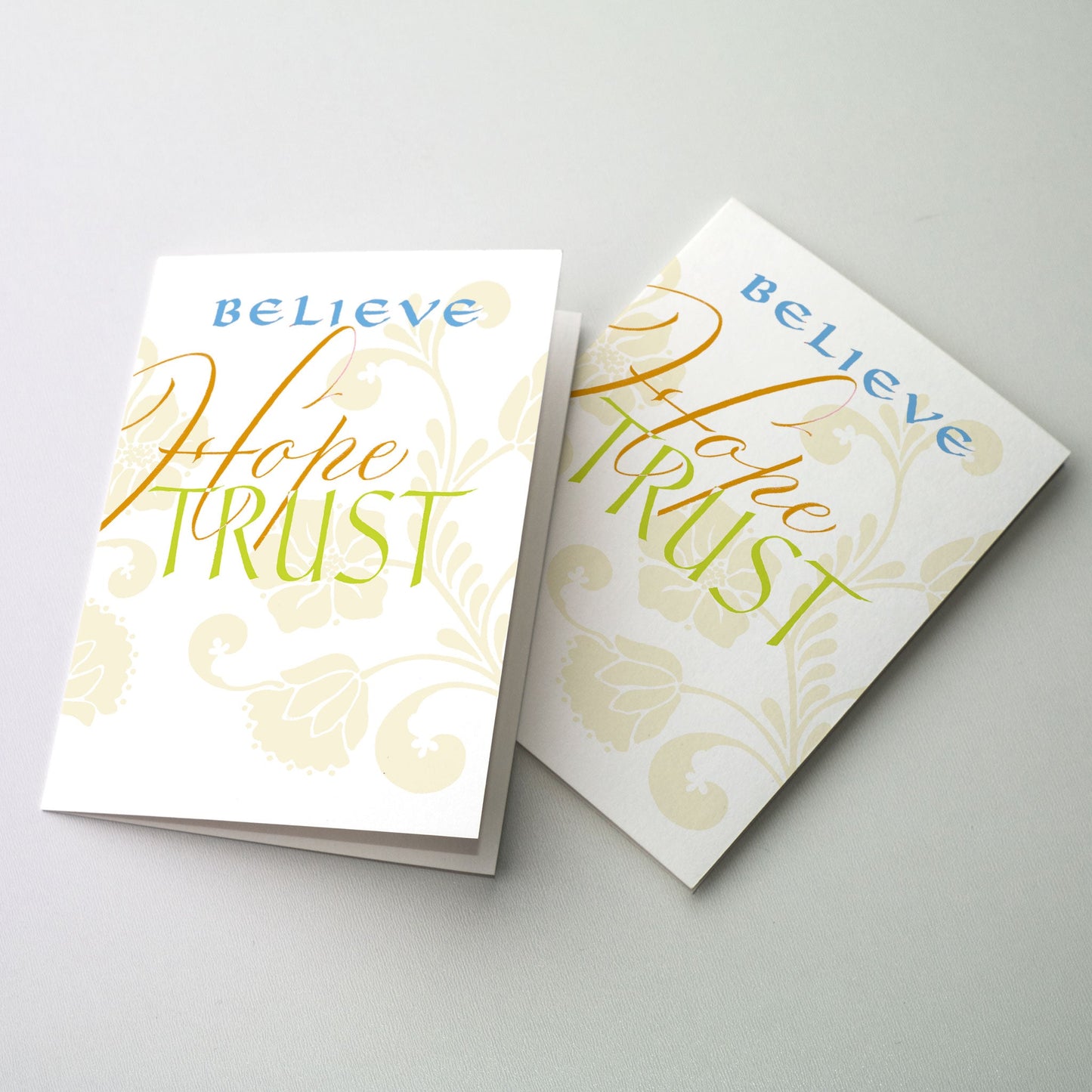 <br>"Believe, Hope, Trust" in blue, deep gold and chartreuse on white ground with light green floral pattern in background.