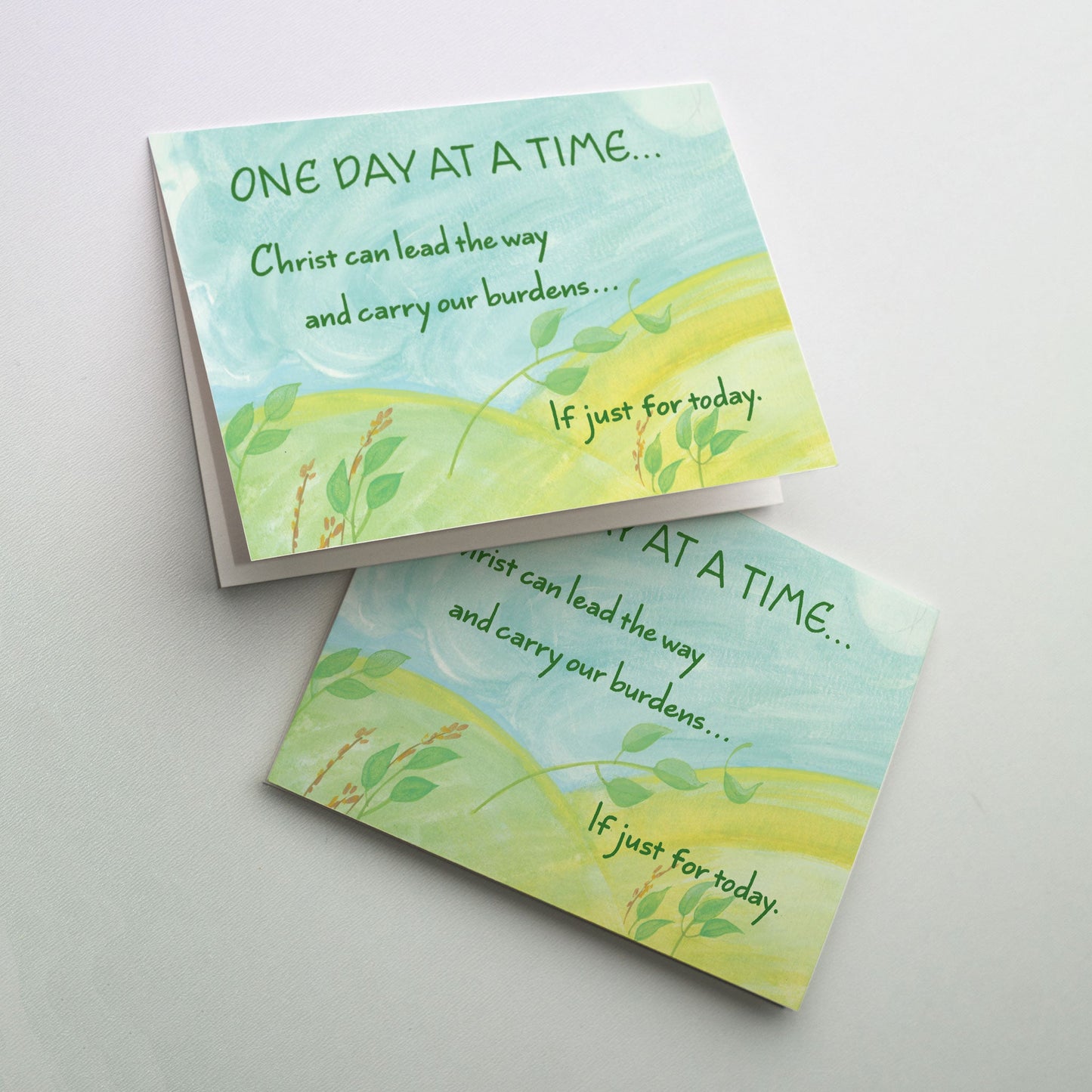 Watercolor of a windy sky over a green landscape of two hills with small green plants bending in the wind. The cards in “One Day at a Time” are reminders that God is there each step of the way during recovery, whether it’s rehab through a 12-step program or recovery from knee or hip surgery.