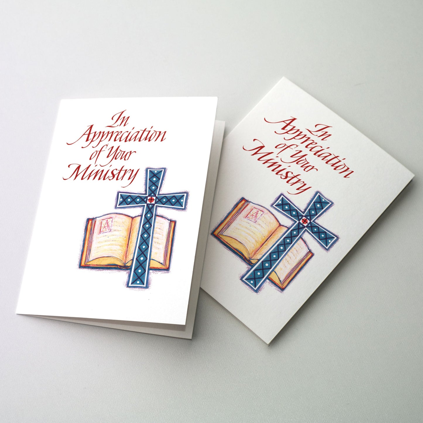 Painted illustration of a blue colored cross with a diamond pattern before an open book of scripture with an illuminated start letter "A". Appropriate as a thank you or retirement card for priests, deacons, other clergy, ministers, or religious.