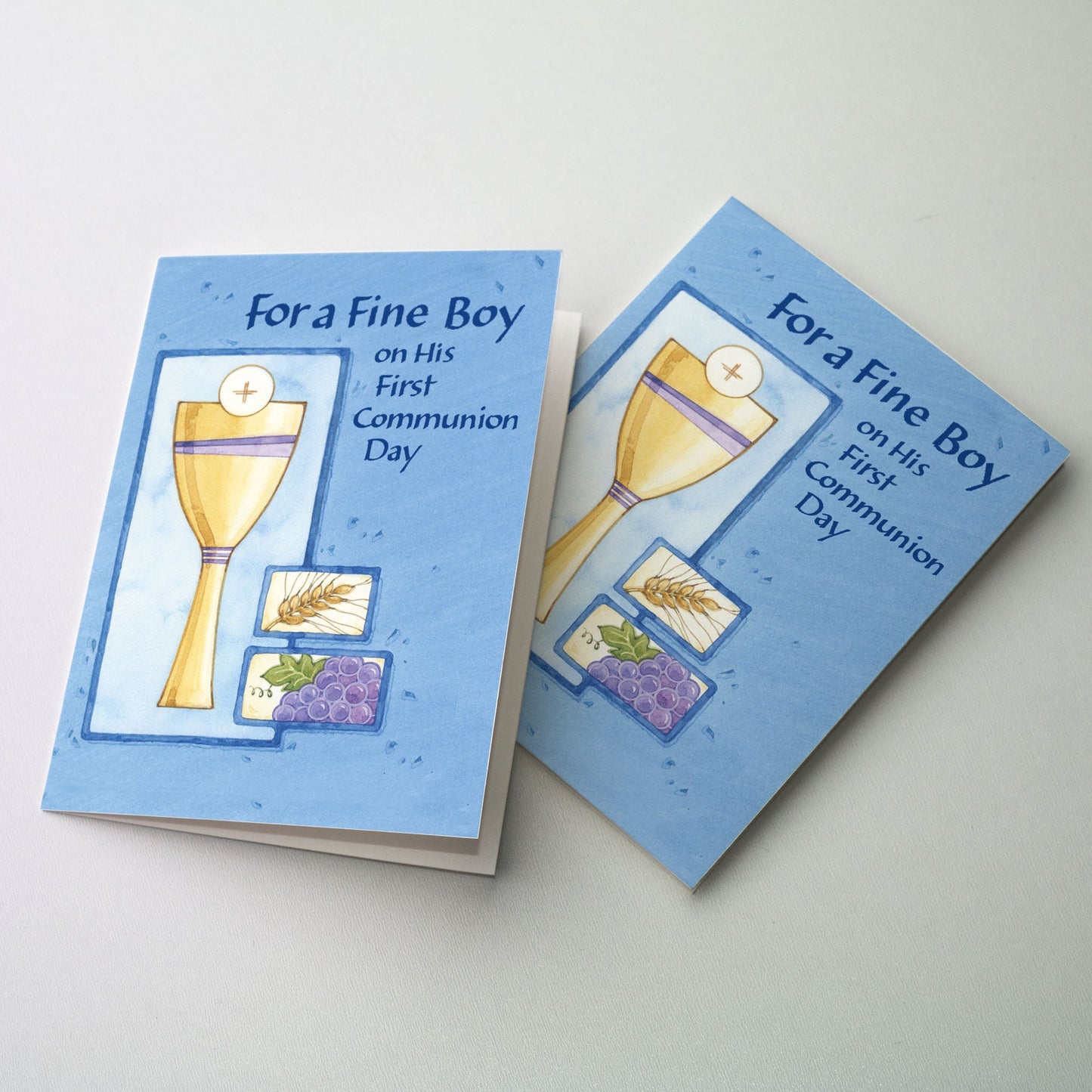 Slender gold chalice with host and inset panels of close-up illustrations of grapes and wheat. Illustrations are bordered with a dark blue frame on a background of lighter blue.